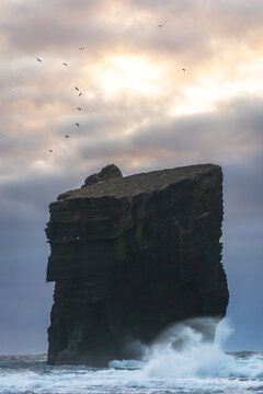 Aerial view of a monolithic rock formation rising from the turbulent sea, waves crashing against its base under a sky streaked with dawn's light, Mosteiros, A&Atilde;&sect;ores, Portugal.