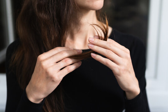 womans hands examine the ends of her long brown hair in close-up. personal care beauty routine health hair damage check concept