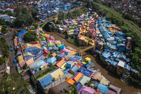 Aerial view of vibrant rainbow-colored houses cascade along the riverbanks, a striking contrast to the lush green foliage, creating a lively urban tapestry, Malang, East Java, Indonesia.