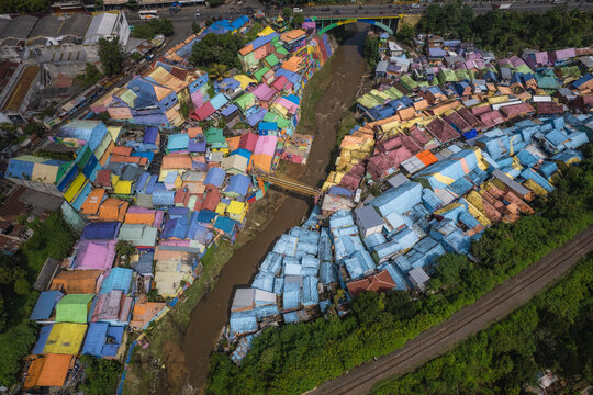 Aerial view of vibrant rainbow hues cascading across the rooftops of colorful houses flanking a muddy river, illuminating the urban landscape, Malang, East Java, Indonesia.