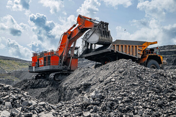 Red excavator loads black coal into back of yellow heavy mining dump truck. Open pit mine process, industry landscape. © Parilov