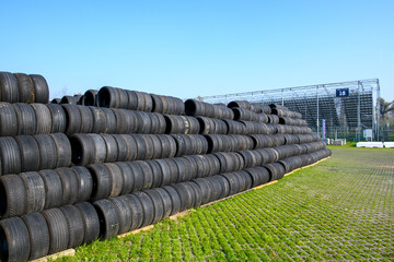 Obraz premium Stacked racing tires forming a safety barrier at Monza racetrack, Italy, under a clear blue sky, conveying speed, motorsport intensity, and track-side atmosphere.