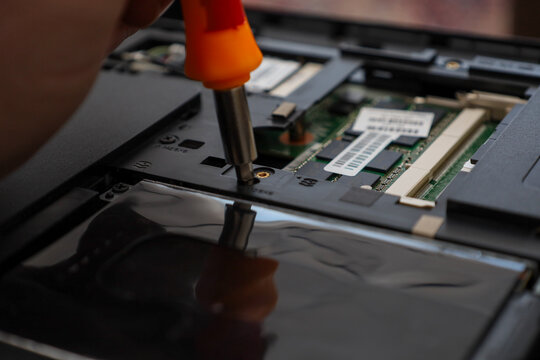 Professional computer repair in a service center using a special screwdriver to disassemble the internal components of a laptop.