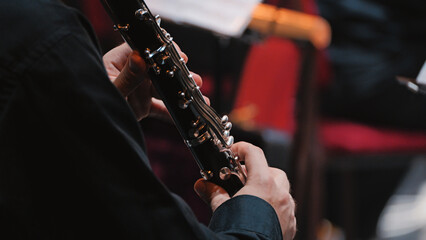 Obraz premium Close-up of a clarinetist's hands on the silver keys of a woodwind instrument during a classical performance. Focused lighting highlights the musician's skill in a concert hall setting