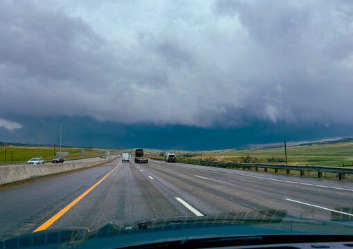View of the highway stretches into the horizon under a brooding, stormy sky, with sparse vehicles punctuating the vast expanse, Winslow, Arizona, United States.