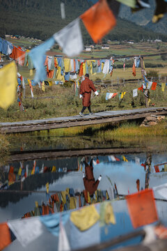 View of a man walking on a wooden bridge over a reflective lake under prayer flags in the valley, Phobjikha Valley, Wangdue Phodrang, Bhutan.