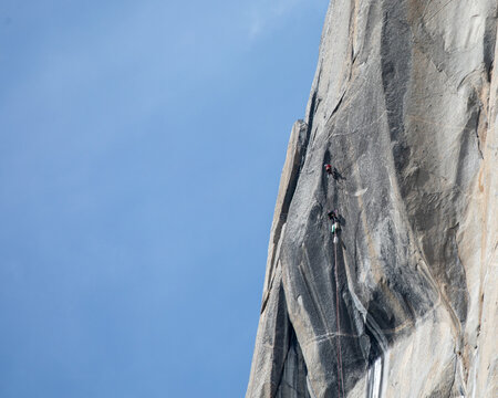 View of granite monolith soaring against a blue sky, with tiny figures of climbers scaling its sheer face, Yosemite Valley, California, United States.