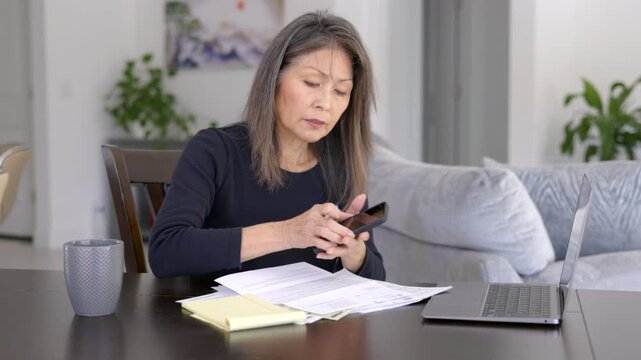 Mature business woman working at home picks up smartphone begins communication sitting at dining room table