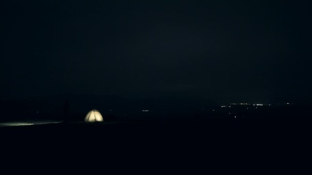 Wild camping scene at night on a hilltop, with a person and a headtorch in cold weather