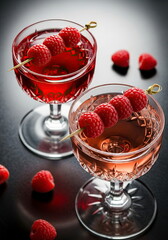 Crystal glasses filled with red cocktails made from ros&eacute; and light pink sparkling wine, decorated with fresh raspberries on the table.