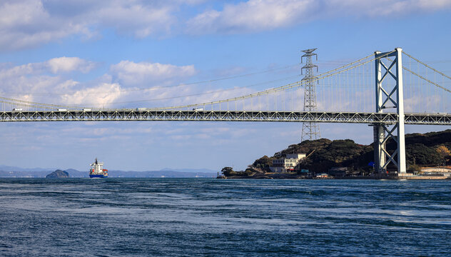 A large ocean liner departed, passing under Kanmon bridge toward the sea at Kitakyushu, Japan.