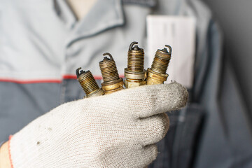 A mechanic holds old spark plugs. Defective spark plugs, stained with motor oil. Soot on the spark plugs.