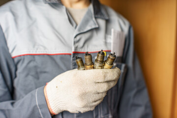 A mechanic holds old spark plugs. Defective spark plugs, stained with motor oil. Soot on the spark plugs.