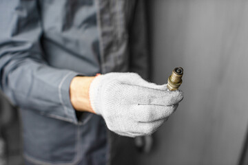 A mechanic holds old spark plugs. Defective spark plugs, stained with motor oil. Soot on the spark plugs.