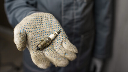 A mechanic holds old spark plugs. Defective spark plugs, stained with motor oil. Soot on the spark plugs.