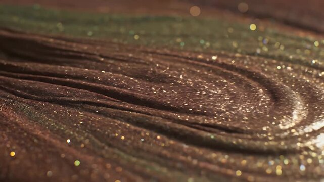 Close up footage of shimmering gold and bronze metallic liquid swirling in slow motion with glittering particles.