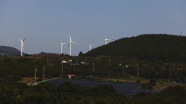 Jeju Island, Jeju-Do, South Korea,  Sinchang Windmill Coastal Road landscape, line of wind mills power generators along the coast, offshore wind farm energy turbines, aerial drone view, green energy