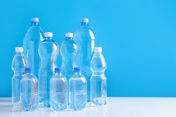 Naklejka premium Water bottles of different sizes on white table against light blue background, space for text