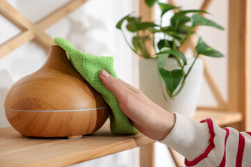 Naklejka premium Woman wiping aroma lamp with microfiber cloth at home, closeup
