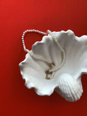 Pearl necklace and seashell on a red background