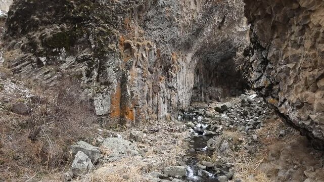 Paved hiking trail passes directly underneath massive natural stone archway inside deep rocky canyon with steep cliffs and patches of white snow during cold cloudy winter day outdoors.

