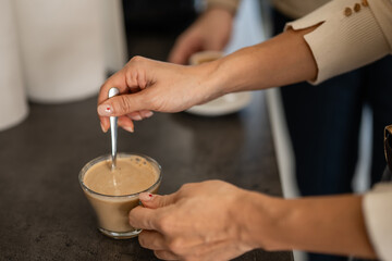 Woman's hands stirring coffee in clear glass cup