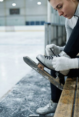 Female figure skater tying laces on ice skates before training