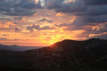 Obraz premium Dramatic Sunset Over Mediterranean Hillside Village with Golden Clouds