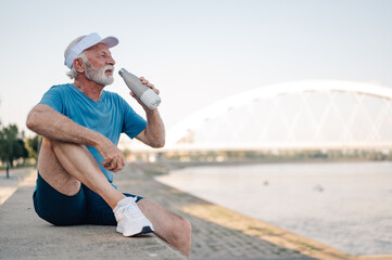 Senior man drinking water after exercising by the river