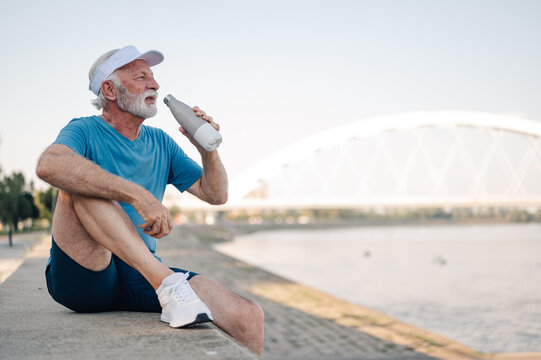 Senior man drinking water after exercising by the river