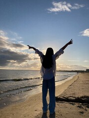 Fototapeta premium Woman Silhouette with Arms Raised on Beach at Sunset