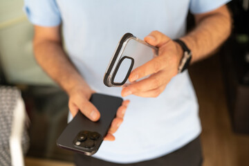 Close-up of a man holding a smartphone and a transparent protective case, preparing to put the case on the phone.