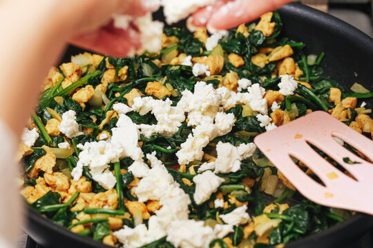Cooking chicken with spinach and feta cheese in frying pan. Homemade healthy meal preparation. Fresh green vegetables with poultry meat. Simple nutritious food cooked at home kitchen.
