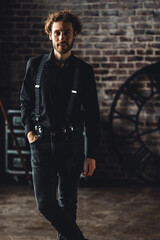 Obraz premium Young sexy handsome fit elegant man in a black shirt looking at camera posing for a photoshoot in a studio. Loft interior, stylish outfit, men's wear, casual clothing. Idea for grooms style, posing