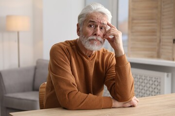 Amnesia. Senior man trying to remember something at wooden table indoors