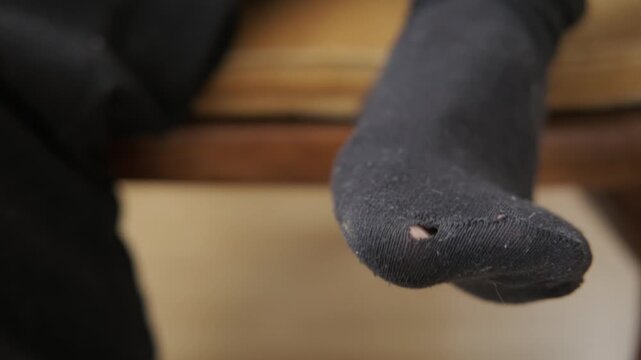 Hole in worn-out sock, worn-out wear, stark reality poverty, Poverty and hardship concept. Close-up on foot with visible hole. Symbol economic struggle