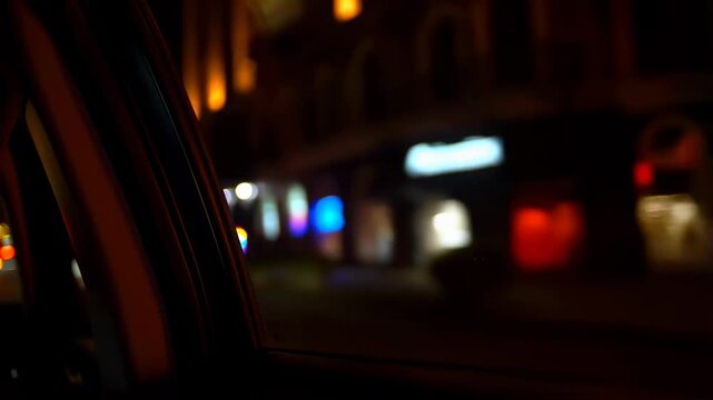 Nighttime city drive with blurred neon signs visible through car window. Capturing the vibrant nightlife and urban atmosphere