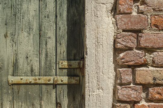 Weathered wooden door with rustic metal hinge in Venice, Italy.