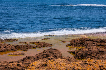 Rocky seashore with small waves washing over coastal rocks and shallow water. Creating a natural seaside landscape that represents ocean, nature, travel, summer and coastal environment concepts.