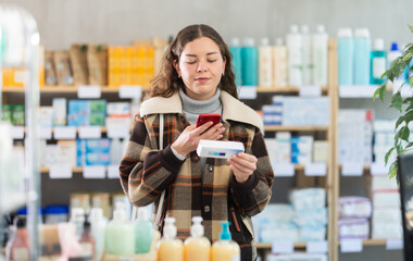 Girl in winter clothes scans code on package of ointment to check the expiration date