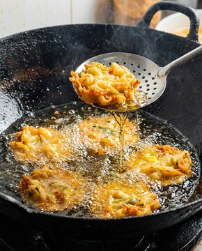 Bakwan vegetable fritters fry in deep bubbling hot oil inside black wok with spoon