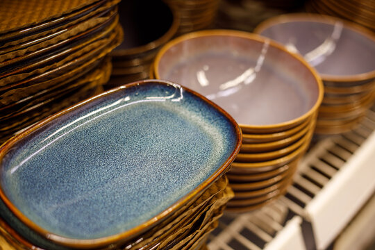 Stacked ceramic plates and bowls with blue glaze on store shelf, handcrafted tableware, modern rustic kitchen dishware, textured pottery close up, warm interior lighting