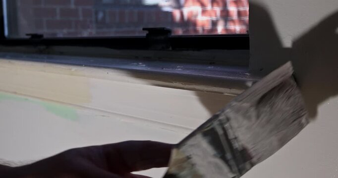 Worker is using paintbrush to apply paint to trim around window work being done.