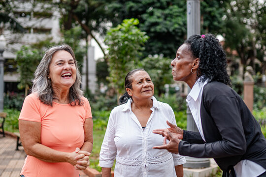 Group of diverse senior women talking and laughing together in a public park.