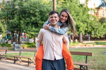 Obraz premium Happy Young Couple Enjoying a Piggyback Ride in a Sunny City Park