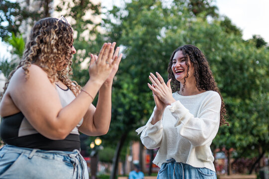 Two Happy Young Women with Curly Hair Playing Hand-Clapping Game in a Sunny Park