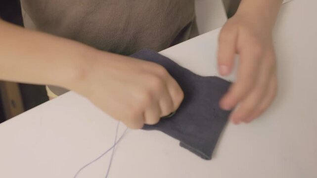 Side angle view of a child sewing by hand, holding cloth and guiding the needle. Calm home environment, learning basic craft skills and developing confidence. Concept of home based education and