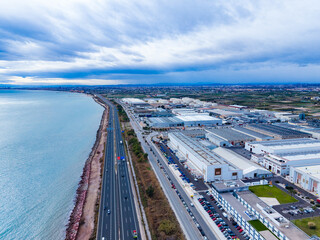 View of a coastal highway and industrial area near the waterfront in an urban location on a cloudy day with some vehicles in motion on the road