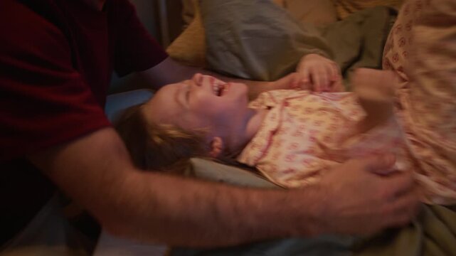 Close up shot smiling and loving Caucasian parents tickling little girl who lying on bed and laughing