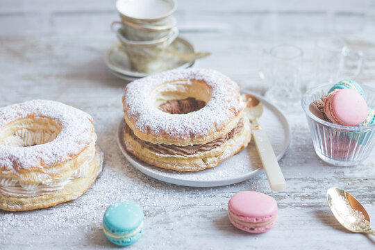 Puff pastry ring filled with chocolate cream and assorted macarons on a table for afternoon tea